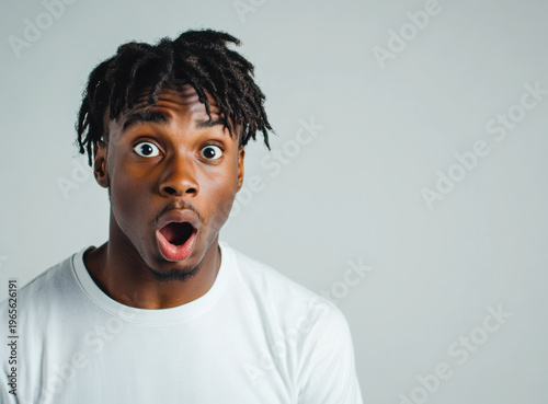 Surprised young man with expressive face standing against plain background