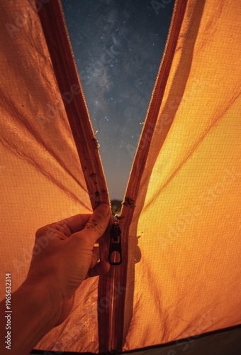 Hand pulling tent zipper at night to reveal the Milky Way starry sky, close up of orange fabric for camping adventure, travel, and outdoor lifestyle gear storytelling