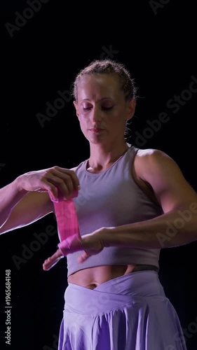 Vertical video, woman pro fighter wraps her hands with pink boxing bandages, boxing training in a dark gym, fighter preparing for hard training, woman power.