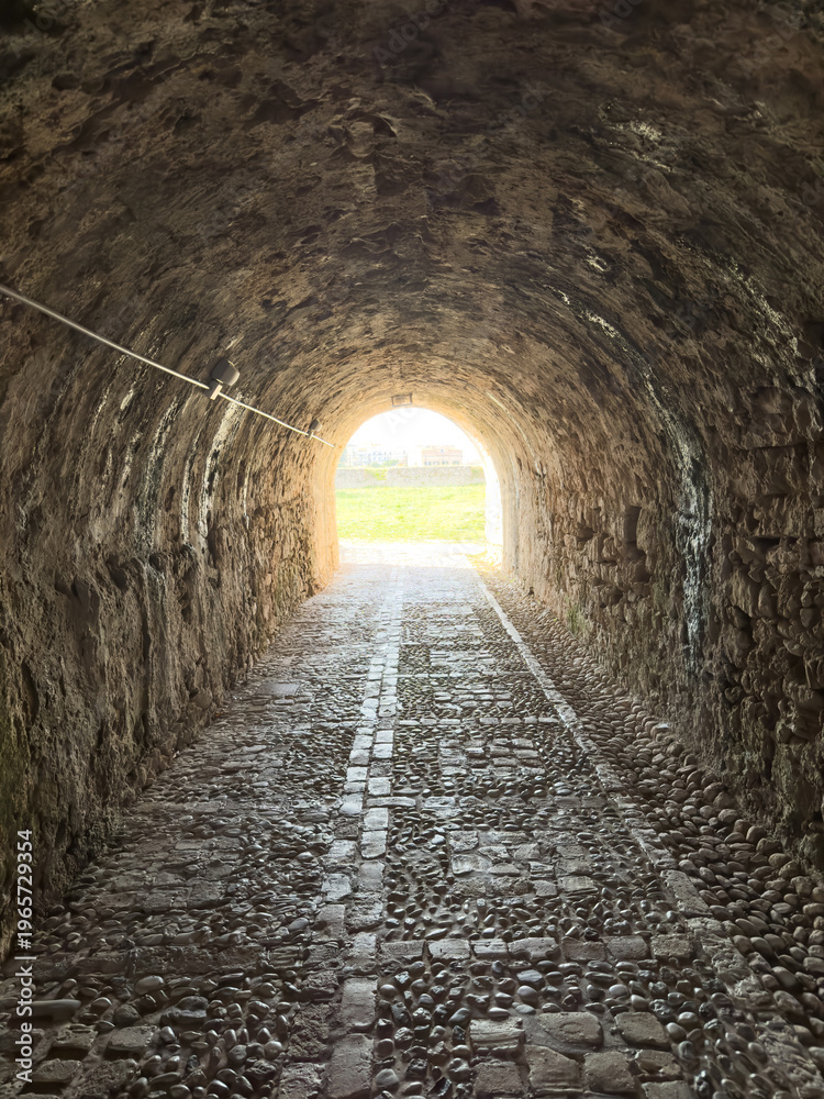 Fototapeta premium Stone tunnel and cobblestone path inside Corfu island New Fortress, Greece. Bright day light at the exit