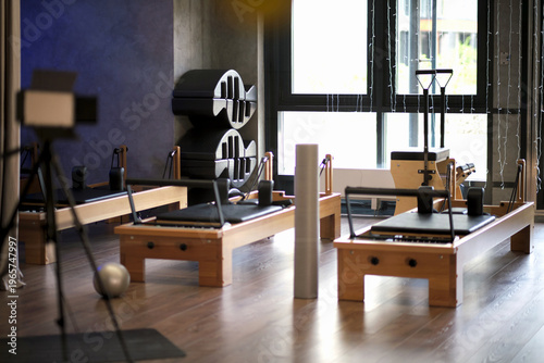 A quiet Pilates studio with reformers, foam roller, and props is shown in soft daylight from a wide interior angle. The clean room suggests mindful workouts, recovery, and modern wellness habits.