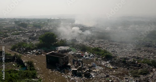 Aerial close-up fly over view. Burning rubbish causing greenhouse gas, contributor to climate change.  Extreme Poverty. People living alongside dumpsite struggling to survive through waste picking.