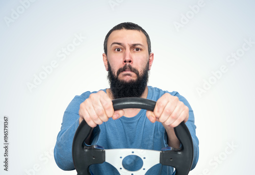 Bearded young man holding car steering wheel and looking focused, driving concept, road control metaphor, transport idea, isolated on light background