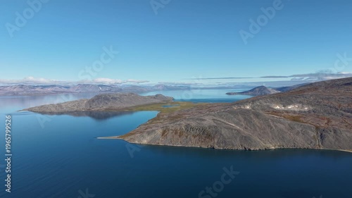 Smooth drift over Rumilet Bay in Chukotka. Tundra peninsula and rocky coast cut into clear blue water. Early autumn calm creates a pristine backdrop for travel, tourism and exploration