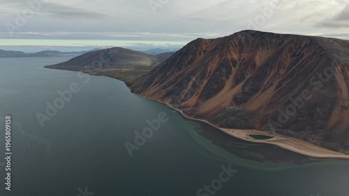Aerial drone footage captures gentle drift over Penkigney Bay coastline near Provideniya. Mountains and tundra fill the horizon in Chukotka . Soft morning light under overcast sky