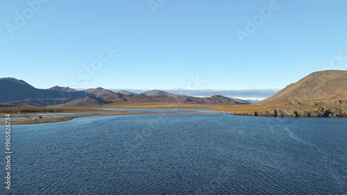 Aerial view reveals a gentle pan along Chukotka bay shoreline and river mouth. Open water and tundra plains stretch to the horizon. Autumn evening light hints at whale habitat and remote adventure