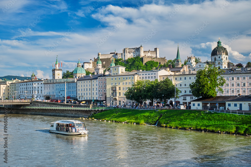Obraz premium Sightseeing boat cruising on the Salzach river with the historic Salzburg city center and fortress on the hill, Salzburg, Austria.