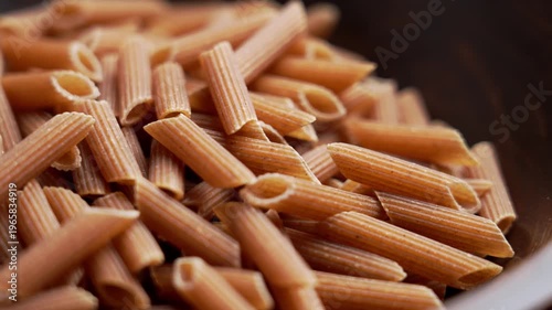 Close up of dry whole grain penne pasta in wooden rustic bowl. Healthy eating concept. Nutritious ingredient of high fiber food