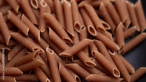 Uncooked whole grain penne pasta falling in slow motion on black ceramic surface. Italian cuisine ingredient. Rotation