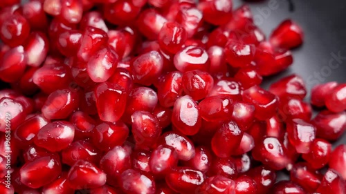 Pile of pomegranate seeds close up. Bright red arils on black ceramic plate. Rotation