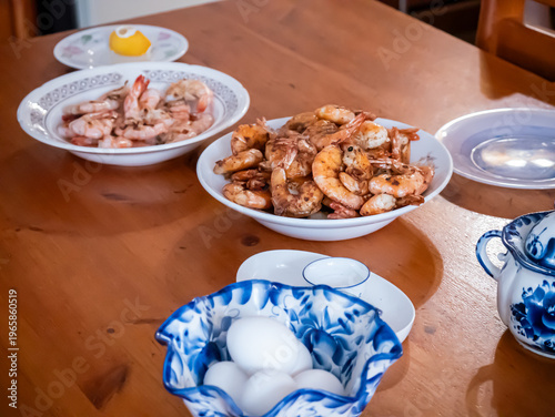 Bowls of cooked shrimp and white eggs on wooden dining table. Homemade meal preparation for healthy dinner. Fresh seafood dish and protein ingredient for kitchen food concept.