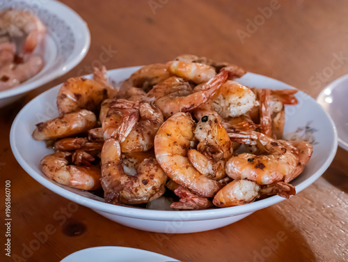 Cooked shrimp in white bowl on wooden table. Fried prawn seasoned with spice for delicious seafood dish. Gourmet meal ready to eat in restaurant. Healthy protein dinner culinary concept.