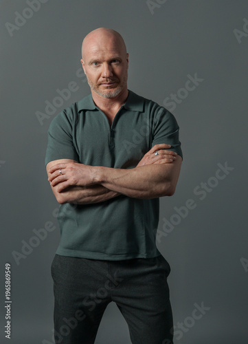 Confident mature bald man in dark green polo shirt looking aside on dark background, studio portrait with dramatic lighting