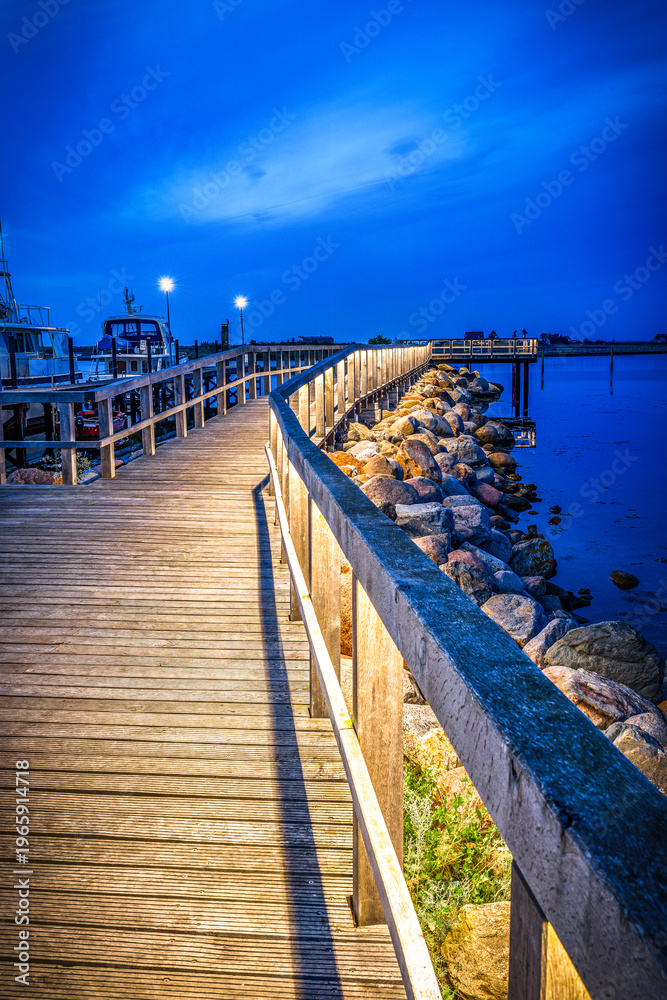 Naklejka premium Illuminated wooden walkway by the sea after sunset at blue hour