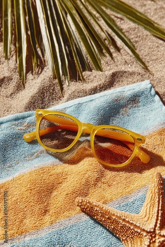 Yellow sunglasses on striped towel with starfish and palm frond