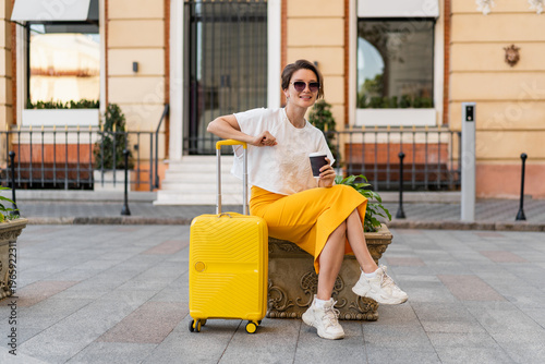 stylish woman traveling with yellow suitcase in Europe