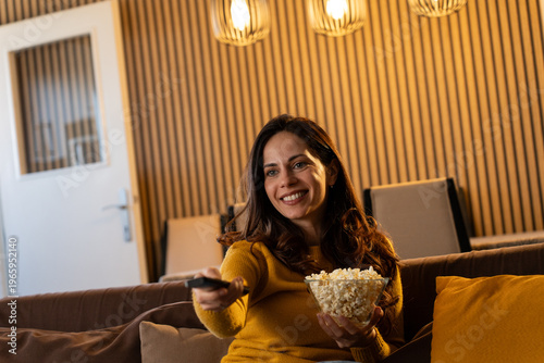 Εκτύπωση καμβά Happy caucasian woman watching TV sitting on the sofa using remote control to change channel