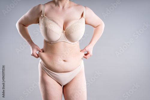 Unrecognizable plus size woman in beige lingerie pinching belly fat. Concept of weight loss, diet and liposuction