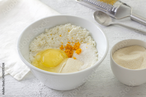 Ingredients for ricotta cheese filling in white bowl with raw egg orange zest semolina and sugar on kitchen table