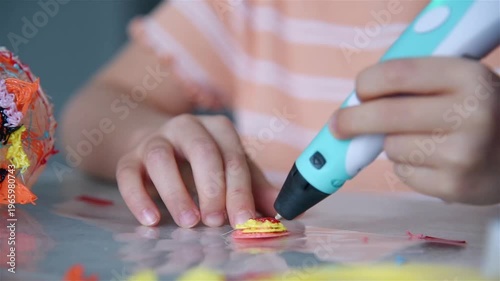 Close up of little girl hands using 3d pen to create plastic shape on table. Creativity education and modern technology concept.