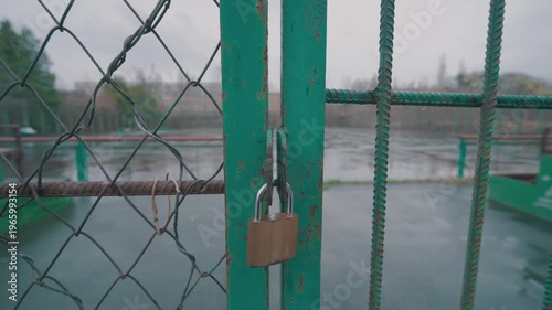Locked Metal Gate with Padlock on Sports Ground | Closed Gridded Entrance in Rainy Gloomy Weather | Restricted Access to Outdoor Stadium During Spring Rain