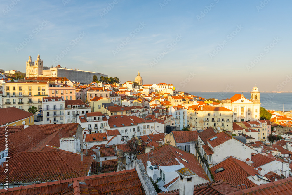 Fototapeta premium Alfama Oldest Historic Neighborhood at Sunset. Red Roofs and White Houses. Vibrant Lisbon Old Town, Portugal. View from Miradouro das Portas do Sol. Wide Shot