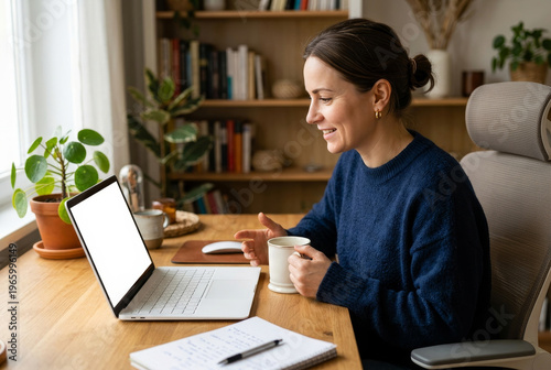 Woman works on laptop while holding cup at home office in the morning