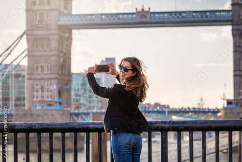 A happy tourist woman taking photos of the famous Tower Bridge in London, England, during her city vacations