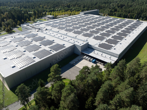 Solar panels cover the roof of a large building in a forested area, supporting renewable energy production for a cleaner future.
