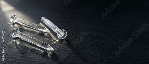 Transparent glass nails lying on dark surface with light reflections, close up abstract objects, industrial concept, minimal design, sharp detail