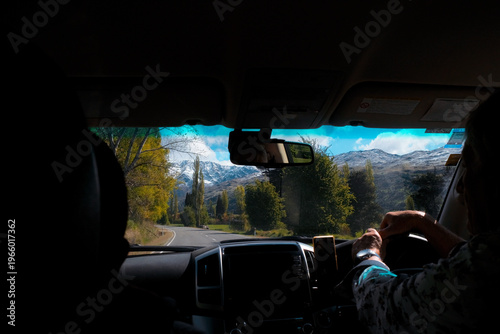 New Zealand Road Trip: POV interior view from a car driving toward snow-capped mountains and autumn trees on a winding highway in the South Island.