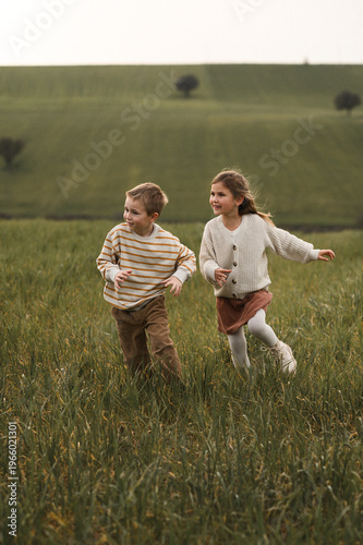 Two children, a boy and girl, playing tag in green fields, running, laughing, and chasing each other, enjoying outdoor fun and sunny summer freedom.