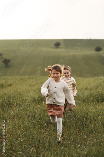 Canvastavla Two children, a boy and girl, playing tag in green fields, running, laughing, and chasing each other, enjoying outdoor fun and sunny summer freedom