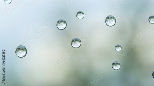 Water droplets on glass create a dreamy effect, blurring a tranquil blue green landscape in the background. Suitable for nature themed designs.