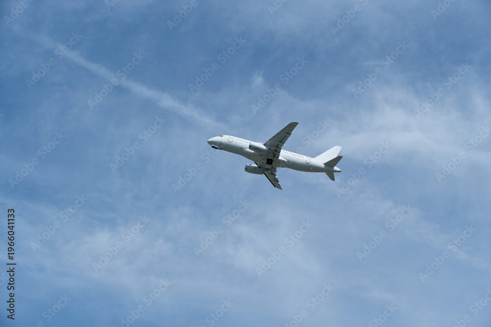Obraz premium White passenger airplane climbing in the blue sky with light cirrus clouds after takeoff. White aircraft taking off and gaining altitude against a beautiful blue sky and wispy clouds.
