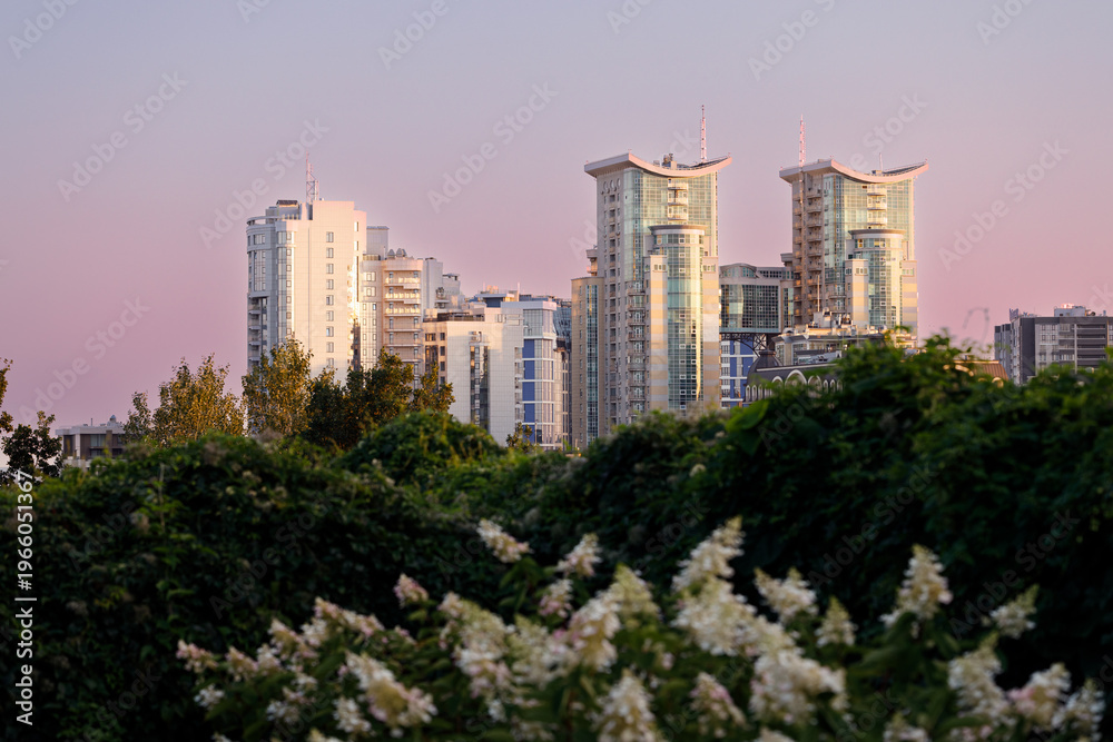 Fototapeta premium Modern city skyline with high-rise buildings and lush greenery at sunset