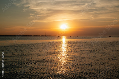 Foto Sunset over water with sailboats in the distance on a warm evening