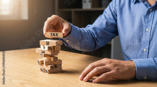 Businessman placing a wooden block with the word tax on top of a tower of blocks, representing tax planning and financial strategy