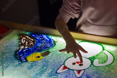 A child's hand draws with sand on a light table, art therapy, sand animation, creative leisure for children, selective focus.