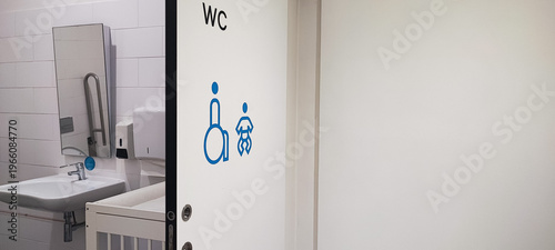 An accessible public restroom with wheelchair and baby changing symbols on the door and safety grab bars inside. Concepts of inclusivity, accessibility, and modern public infrastructure design.