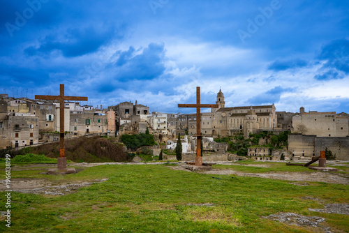 Wooden three crosses (with fallen one) on a hill in middle ages town with a heavy blue rainy sky - crucifixation on catholic Easter