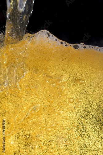 Beer. Jet of beer is poured into a beer glass, causing a lot of bubbles and foam. Beer background