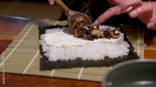 Female hands are cutting a sushi roll with nori algae seaweed and rice on a chopping board with a sharp knife. Different healthy ingredients are enclosed in the Japanese food roll. Healthy homemade fo