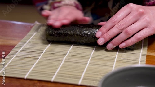 Homemade sushi roll nori algae getting wetted and closed by hands horizontal