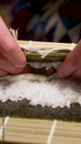 Homemade sushi roll formed with bamboo mat and hands vertical