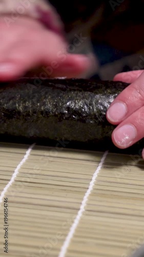 Homemade sushi roll nori algae getting wetted and closed by hands vertical