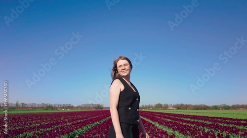 Woman turns her body slowly among rows of tulips under clear blue sky, relaxed outdoor scene, spring bloom, lifestyle moment in nature.