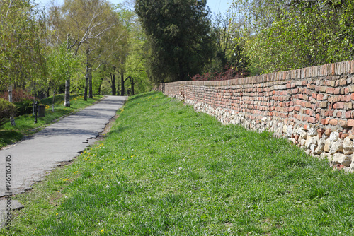 Brick and Stone Wall Grass Lawn Walk Path in City Park Spring
