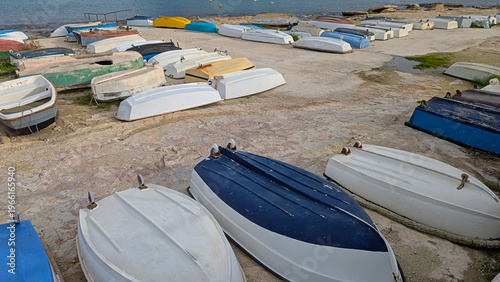 Canvas Print Small dinghies and rowboats arranged upside down on rocky waterfront near calm w