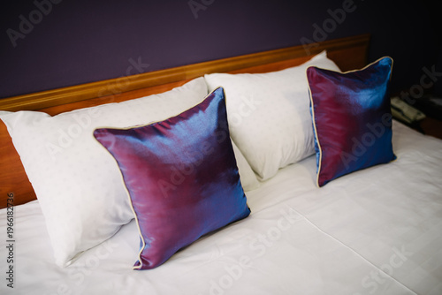 Decorative pillows on bed with white linens and purple wall background